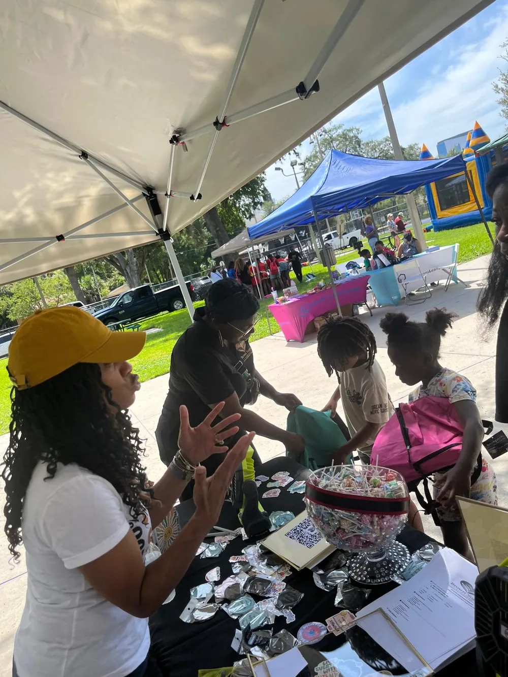 A volunteer handing a pink backpack and a teal backpack to two children at the supply table