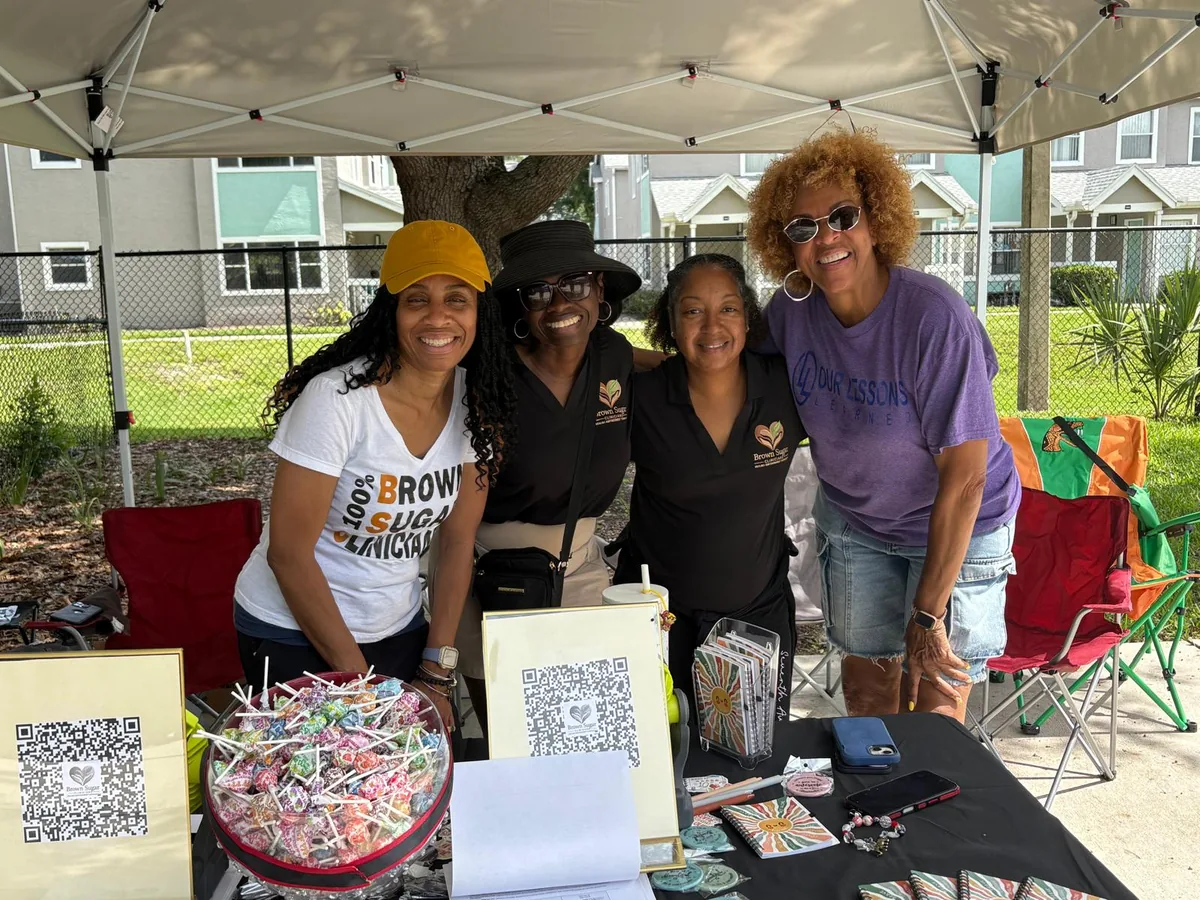 Four women from Our Lessons Learned and Brown Sugar Clinical Services standing together at their table