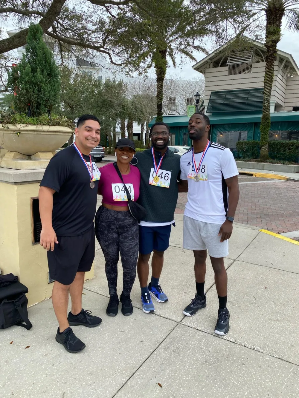 Four run & walk participants wearing race bibs and finisher medals at Harbor Park